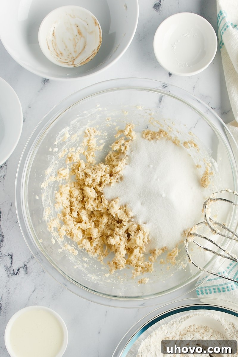 Overhead view of sugar added to butter in a mixing bowl.