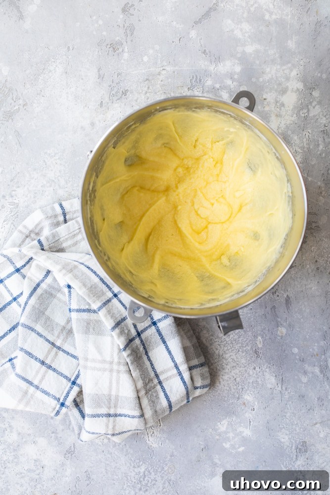 Overhead view of cake batter in a mixing bowl with a tea towel beside it, showing the creamy texture.