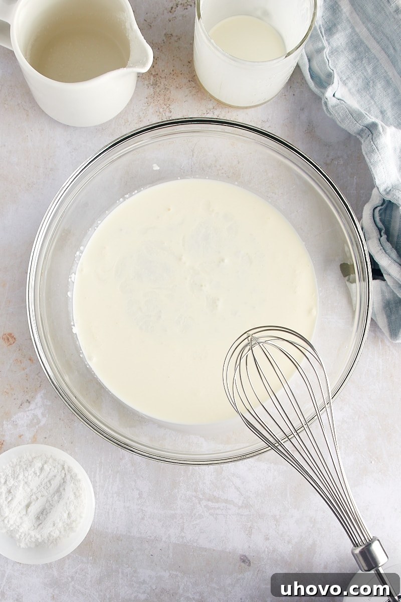 overhead view of cold heavy cream and coconut milk in a large glass mixing bowl, ready to be whipped