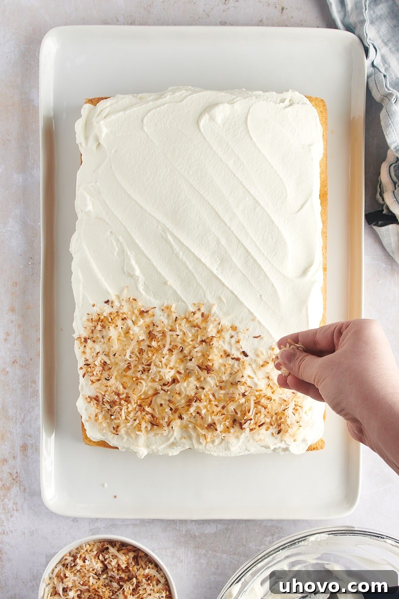 overhead view of toasted coconut being generously sprinkled over the whipped cream frosted coconut cake