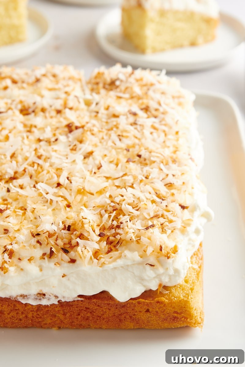 Coconut Sheet Cake on a white serving tray with several slices on plates arranged in the background