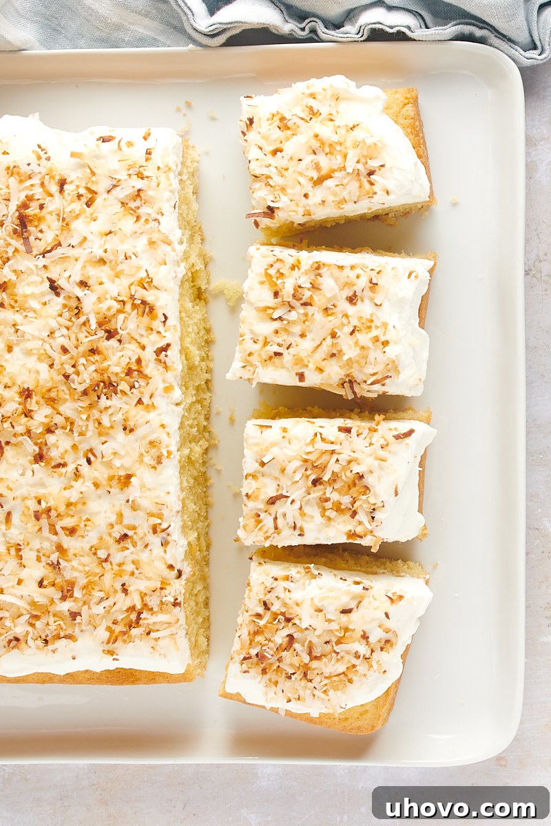 overhead view of partially sliced Coconut Sheet Cake on a white serving tray, revealing its fluffy texture