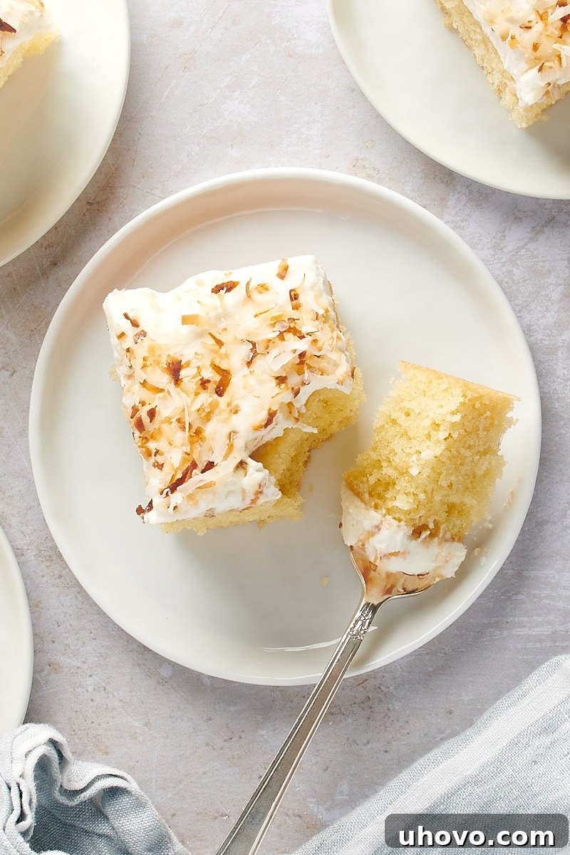 overhead view of a slice of Coconut Sheet Cake on a white plate with a bite on a fork, ready to be enjoyed