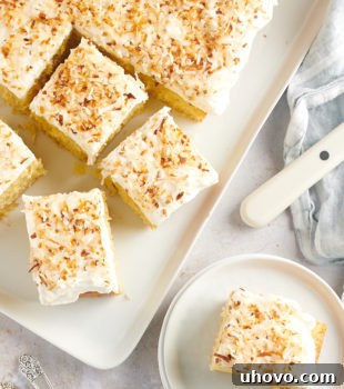 overhead view of Coconut Sheet Cake on a white serving tray and a slice on a white plate