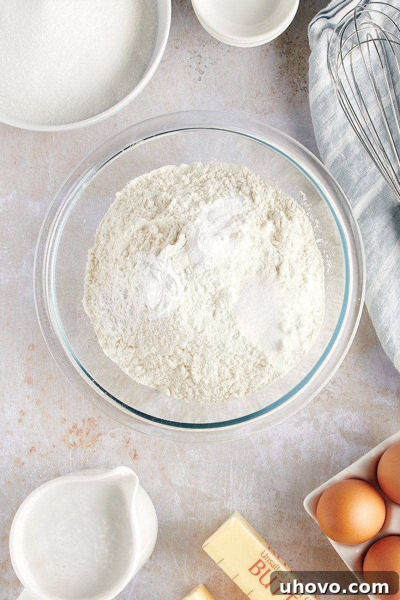 overhead view of flour, baking powder, baking soda, and salt measured in a glass mixing bowl
