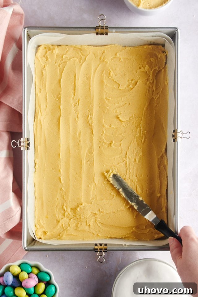 overhead view of sugar cookie dough being evenly spread in a 9x13 pan, forming the base of the bars