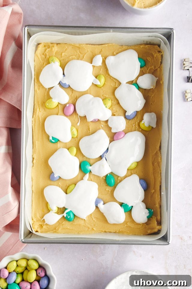 overhead view of marshmallow creme dolloped over the top of sugar cookie dough and M&Ms in a 9x13 pan