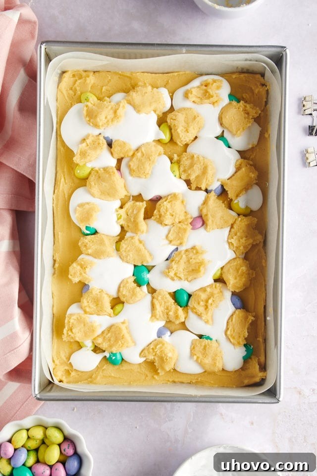 overhead view of assembled M&M Marshmallow Sugar Cookie Bars, layered with dough, M&Ms, marshmallow creme, and reserved dough, ready to bake