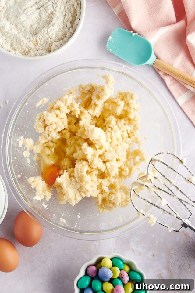 overhead view of an egg being added to the creamed butter and sugar mixture in a glass mixing bowl