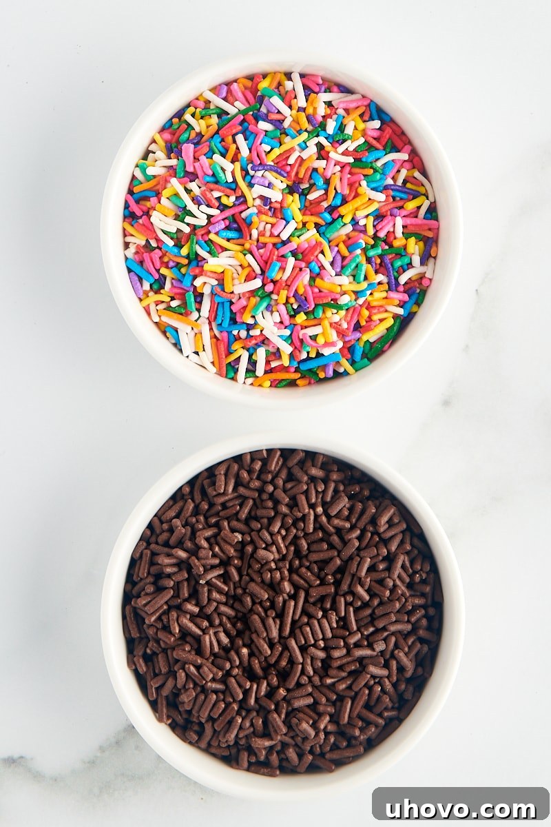 overhead view of rainbow jimmies and chocolate jimmies in white bowls on a marble surface