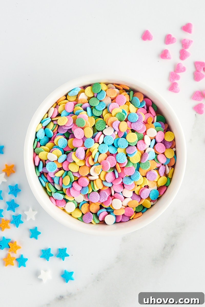 overhead view of quins sprinkles in a white bowl with more sprinkles scattered around the bowl