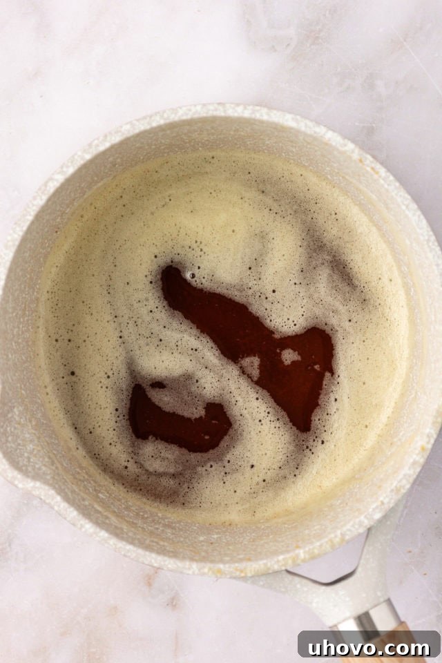 Overhead view of unsalted butter cubes gently melting and beginning to foam in a saucepan, the first step to achieving rich brown butter for snickerdoodles.