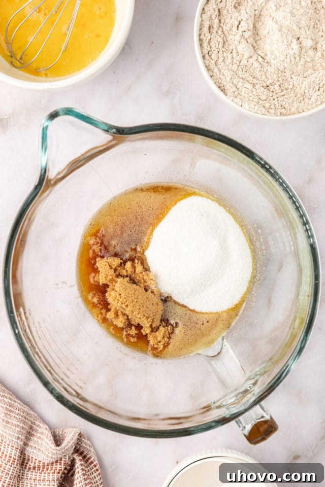 Granulated sugar and light brown sugar being added to the cooled, browned butter in a mixing bowl, illustrating the next step in preparing the snickerdoodle dough.