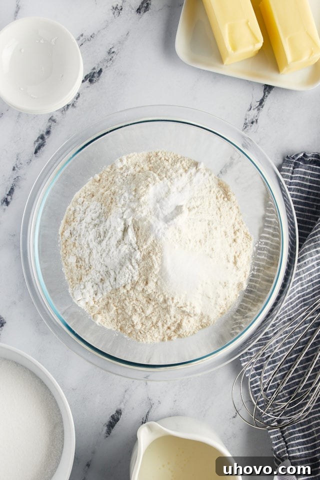 Overhead view of all-purpose flour, baking powder, baking soda, and salt measured in a clear glass mixing bowl, ready to be combined.
