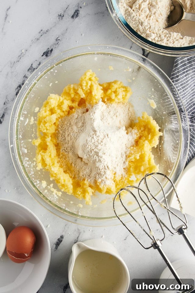 Overhead view of a portion of the dry ingredients being added to the wet ingredients in a glass mixing bowl for Southern tea cakes.
