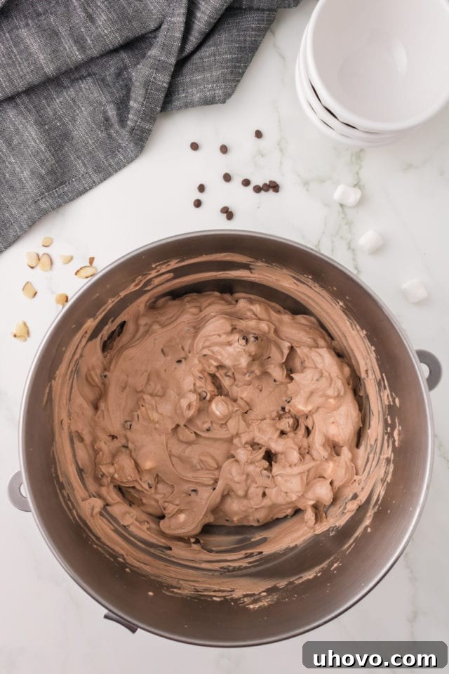 A close-up overhead view of the perfectly mixed Rocky Road ice cream in a metal mixing bowl, revealing a delightful blend of chocolate base, marshmallows, and almonds.