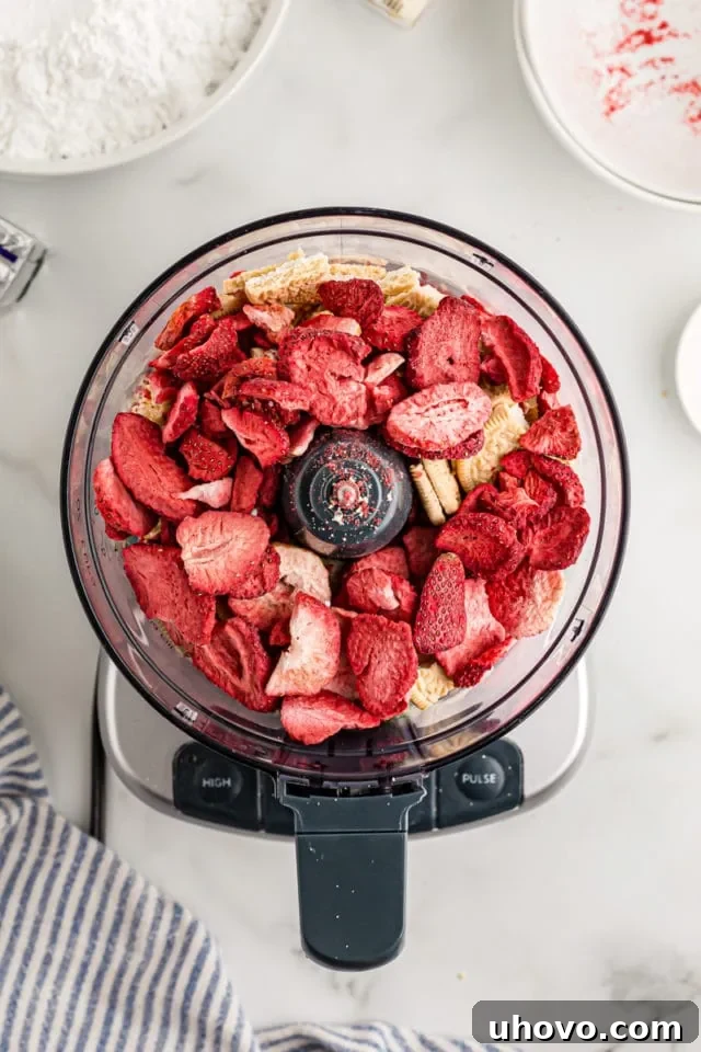 Overhead view of Golden Oreos and freeze-dried strawberries placed in a food processor, ready to be pulsed into crumbs.