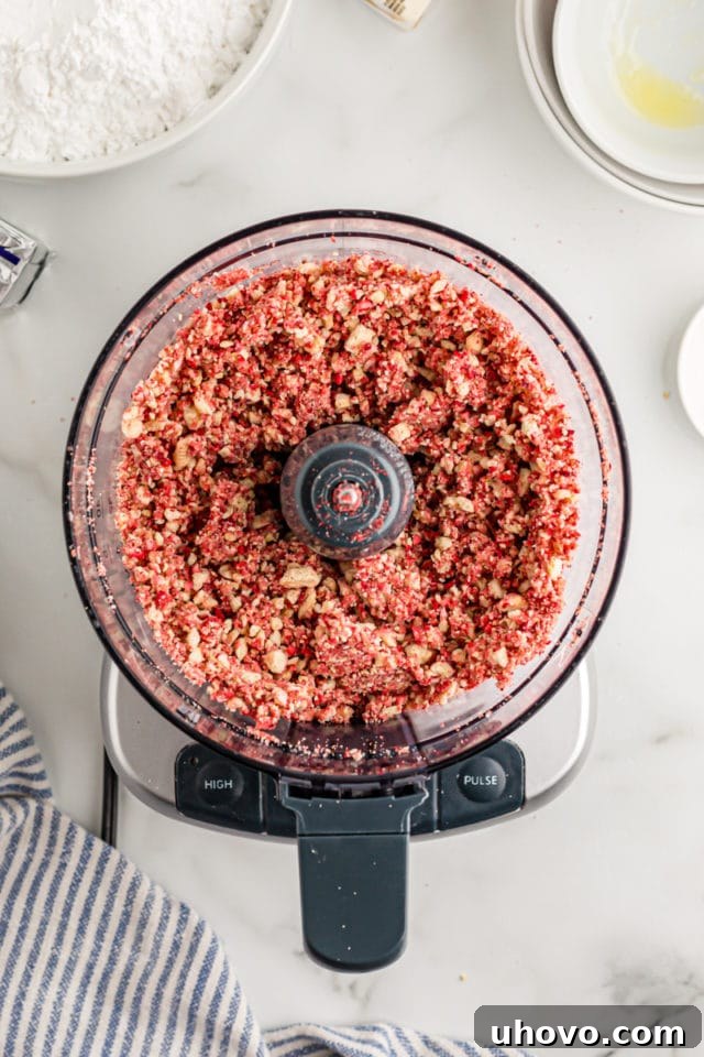 Overhead view of melted butter being mixed into the strawberry crunch mixture in a food processor, helping to bind the crumbs.