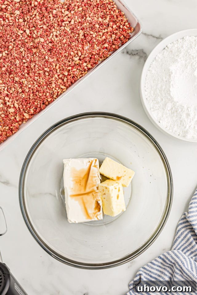 Overhead view of softened cream cheese, butter, and vanilla in a glass mixing bowl, ready to be beaten.
