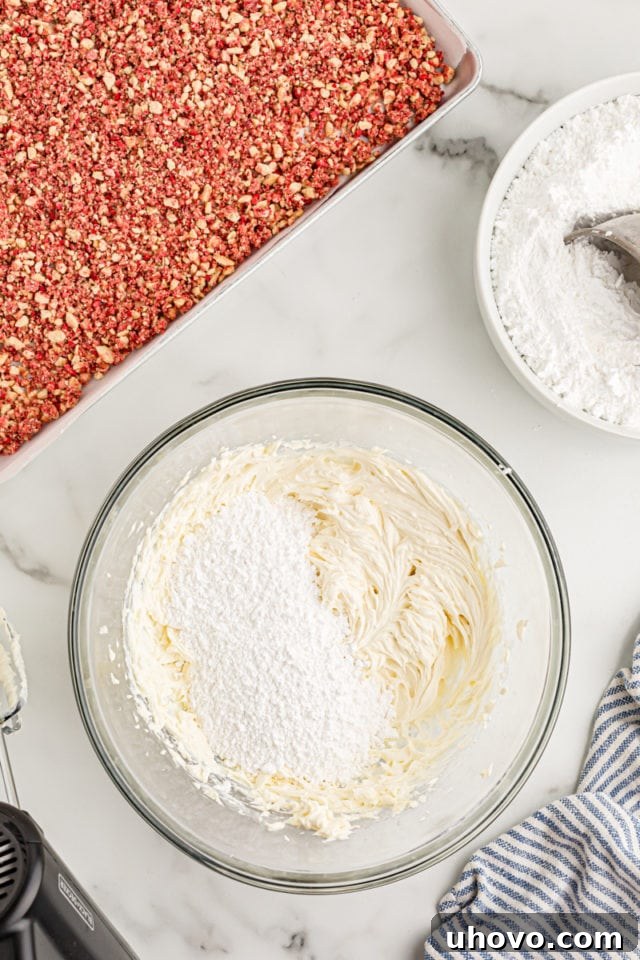 Overhead view of confectioners' sugar being gradually added to the mixing bowl containing creamed butter and cream cheese for the frosting.