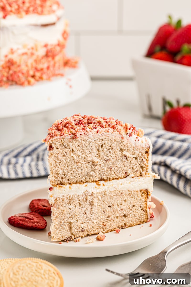 A perfect slice of strawberry crunch cake on a white plate, showing the distinct layers of cake, frosting, and crunchy topping, with a fresh strawberry garnish.