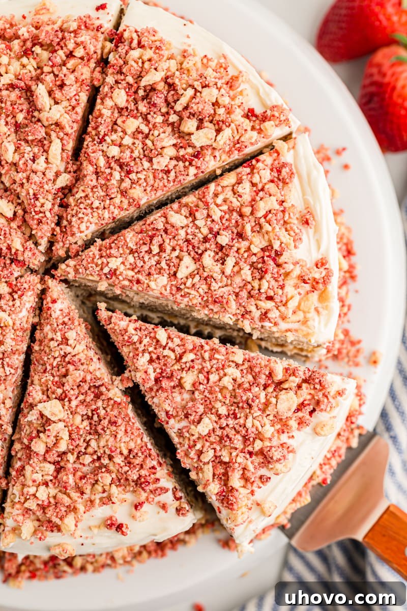 Overhead view of a large platter with a sliced strawberry crunch cake, showing one slice being removed, garnished with fresh strawberries.