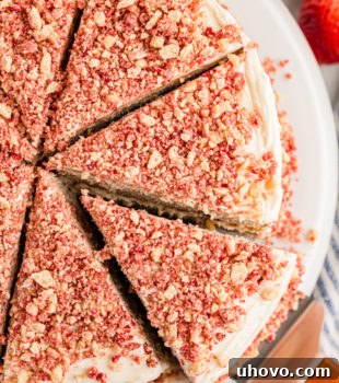 Overhead view of sliced strawberry crunch cake on platter with one slice being removed