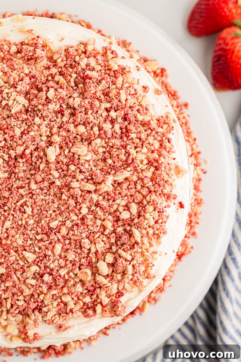 Overhead view of a whole strawberry crunch cake on a white cake pedestal, garnished with fresh strawberries and extra crunch topping.