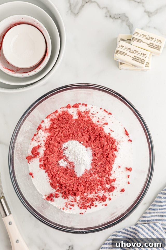 Overhead view of dry ingredients for the cake, including flour, sugar, and ground freeze-dried strawberries, in a mixing bowl before whisking.