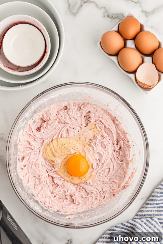 Overhead view of an egg cracked into a bowl of cake batter, ready to be mixed in.