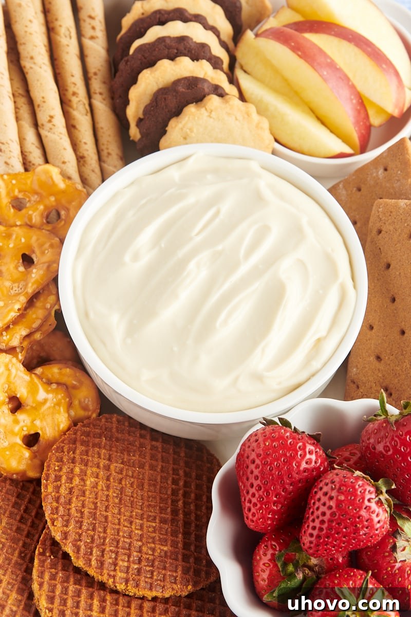 A beautifully arranged bowl of creamy cheesecake dip, surrounded by an assortment of delicious dippers like fresh berries, graham crackers, and various cookies, on a rustic serving board. Perfect for a party or dessert spread.