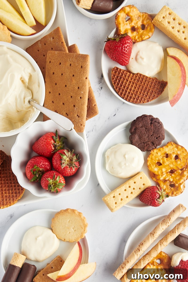 An overhead shot showcasing a beautifully arranged dessert board, featuring a central bowl of cheesecake dip surrounded by an array of colorful fresh fruits, various cookies, and crunchy crackers, perfect for sharing at a gathering.
