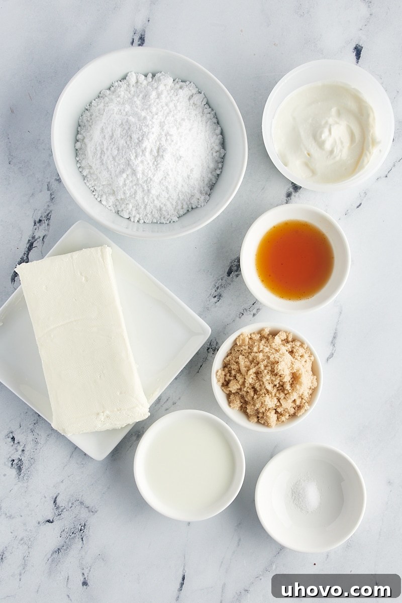 An overhead view of all the fresh, high-quality ingredients laid out on a clean counter, ready to be combined for the no-bake cheesecake dip. Ingredients include blocks of cream cheese, a tub of sour cream, measuring cups of powdered sugar and brown sugar, a bottle of vanilla extract, and a glass of milk.