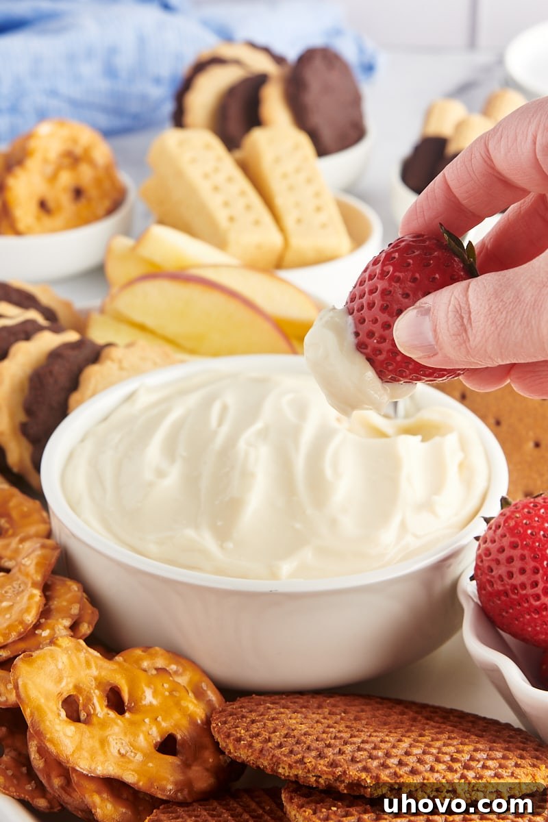 A hand gracefully dipping a vibrant red strawberry into a luscious, creamy bowl of cheesecake dip, highlighting the perfect pairing of fresh fruit and rich dessert.