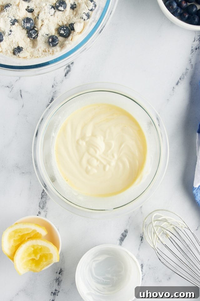 A close-up, overhead shot of the whisked wet ingredients for blueberry scones – Greek yogurt, egg yolk, and lemon juice – combined in a glass bowl, forming a smooth mixture.