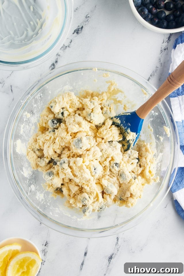 An overhead shot of mixed blueberry scone dough in a glass mixing bowl, showing it just starting to come together after the wet ingredients have been added, with blueberries visible.