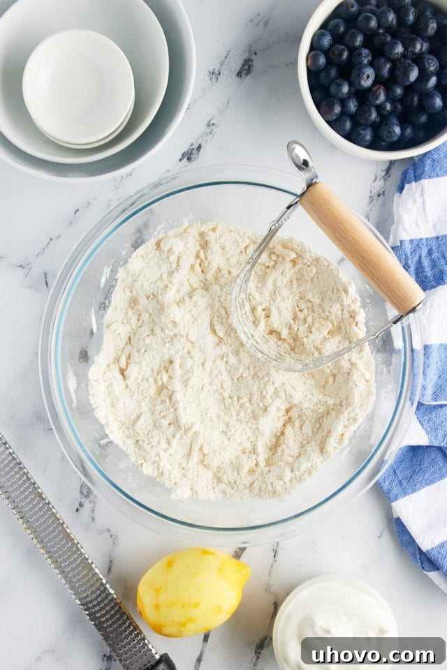 A top-down view of partially mixed blueberry scone dough in a glass bowl, showing the butter cut into the dry ingredients, creating a crumbly texture.