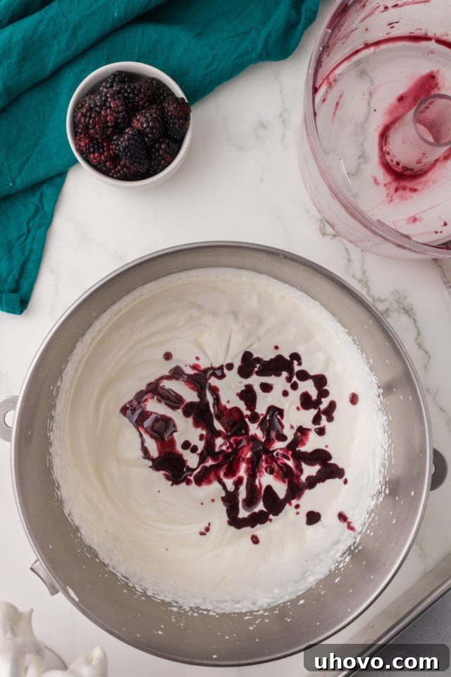 overhead view of blackberry puree being added to lightly whipped cream in a metal mixing bowl