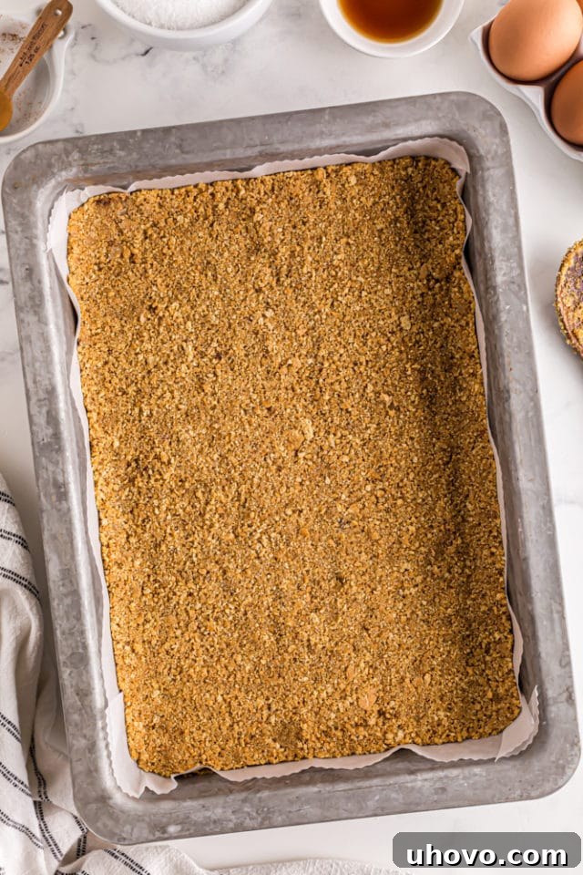 Overhead view of the graham cracker crust meticulously pressed into a 9x13 inch baking pan, lined with parchment paper for easy removal.
