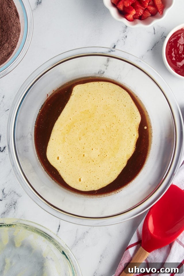 Overhead view of the egg and sugar mixture being poured into the bowl of melted chocolate and butter, ready to be combined.