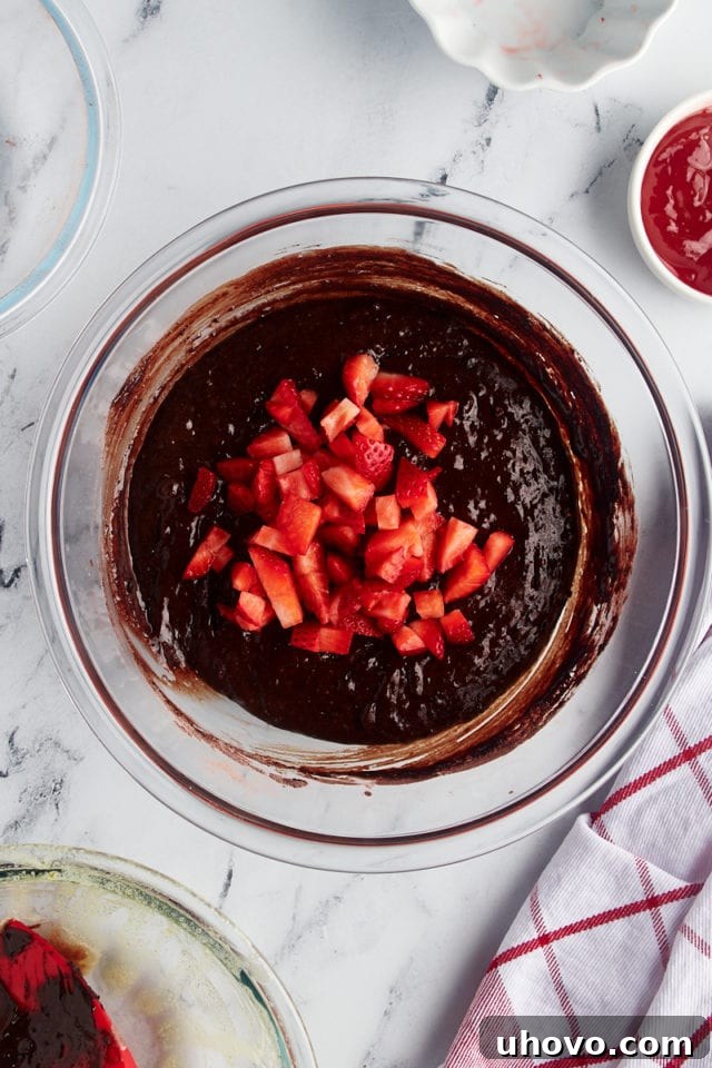 Overhead view of diced fresh strawberries gently folded into the rich brownie batter in a mixing bowl.