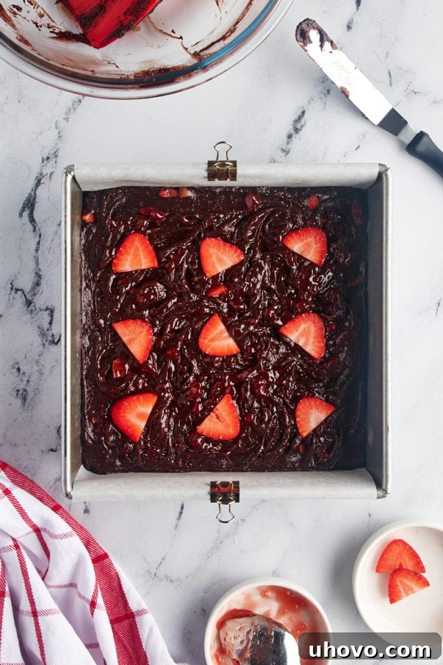 Overhead view of the unbaked strawberry brownies in the prepared pan, showcasing the jam swirls and fresh berries.