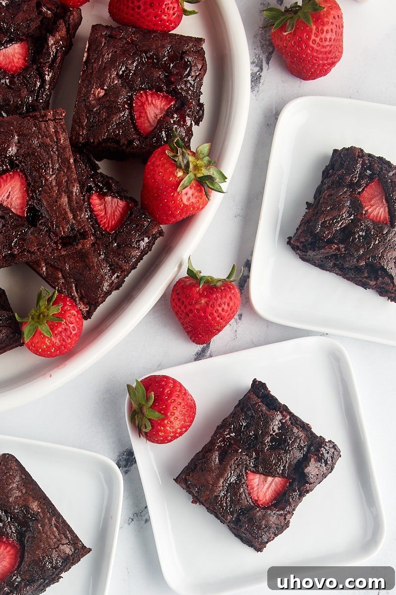 Overhead view of strawberry brownies on three square plates and a platter, ready to be served and enjoyed.