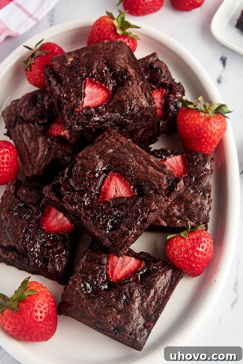 Overhead view of multiple strawberry brownies on a serving platter with scattered fresh berries, highlighting their vibrant appeal.