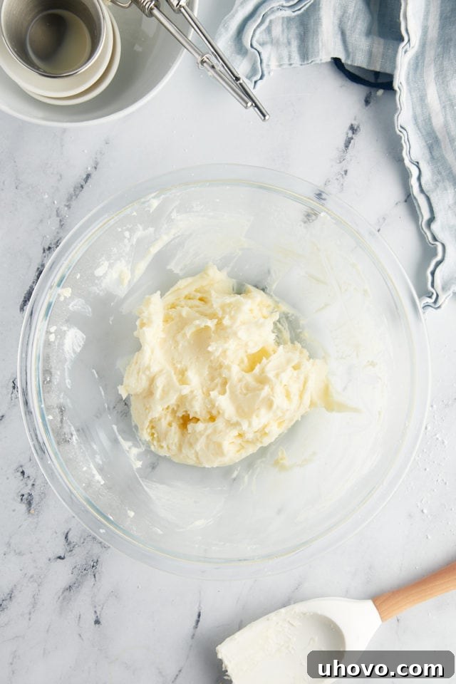 Overhead view of smooth, fluffy vanilla frosting expertly mixed and resting in a clear glass mixing bowl, showcasing its creamy texture.