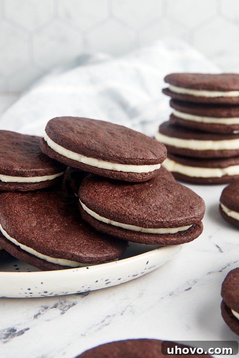 A pristine white plate holds several homemade Oreos, with a stack of more delicious cookies visible in the background, highlighting their fresh appearance.