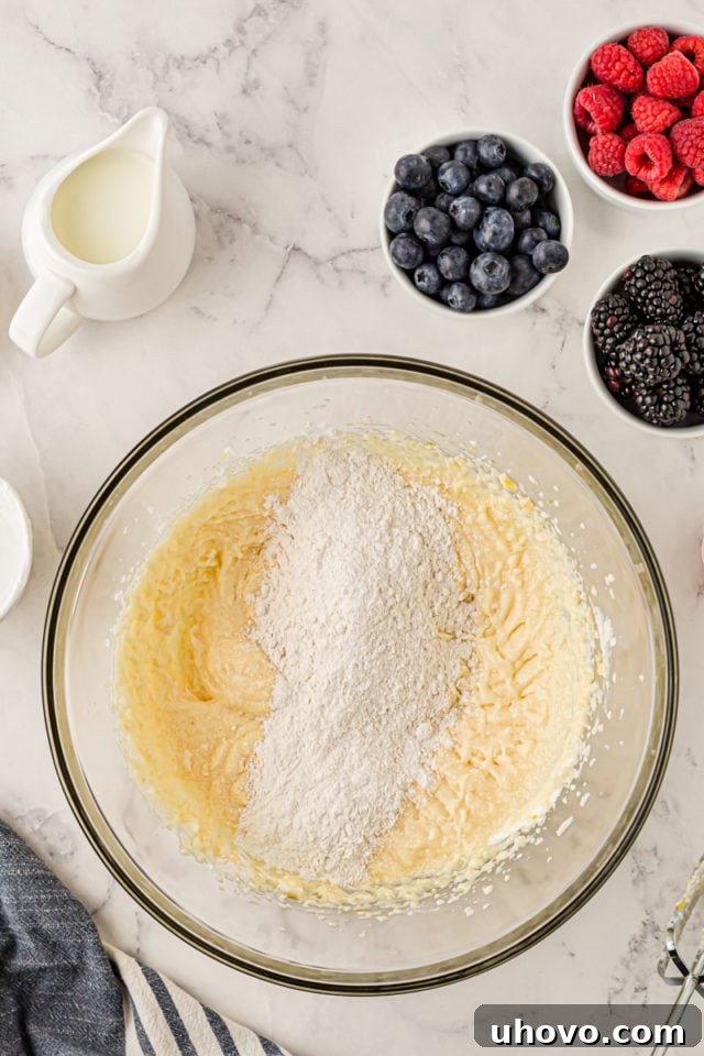 An overhead view of the dry ingredients being carefully added to the wet ingredients in a glass mixing bowl, demonstrating the alternating mixing technique for cupcake batter.