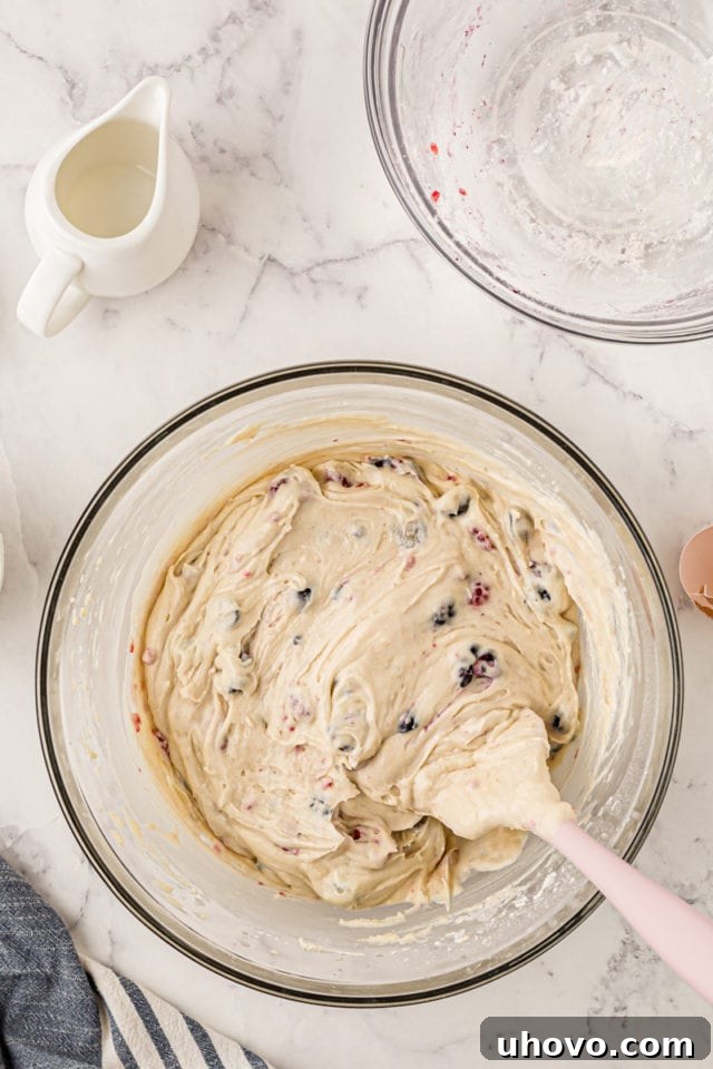 A vibrant overhead shot of the finished berry cupcake batter, flecked with colorful blueberries, raspberries, and blackberries, ready to be portioned into muffin cups.