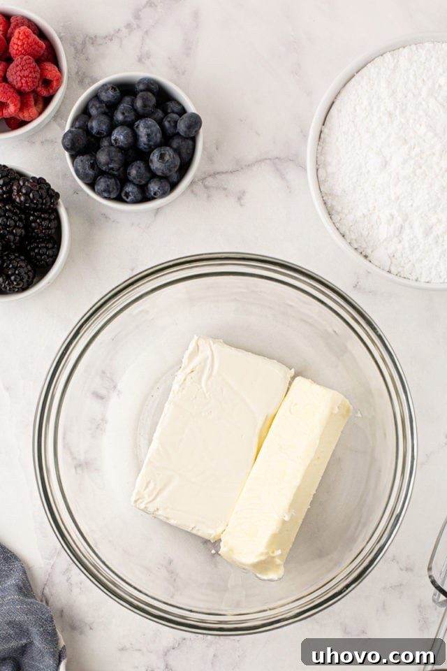 An overhead view of softened butter and cream cheese in a glass mixing bowl, ready to be beaten together for the creamy frosting.