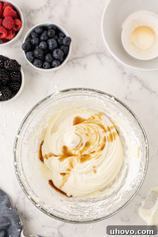 An overhead view of vanilla extract being mixed into the creamy cream cheese frosting in a glass bowl, adding a final touch of flavor.